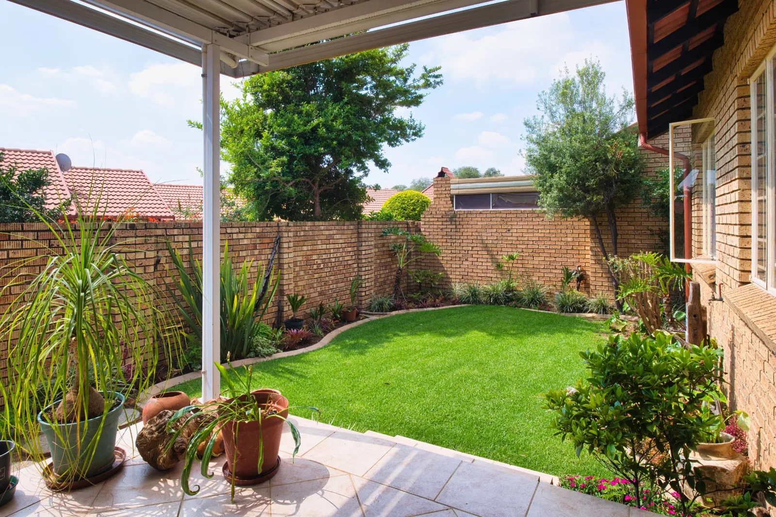 Artificial turf lawn in a walled suburban garden with tiled patio, planted borders and pot plants