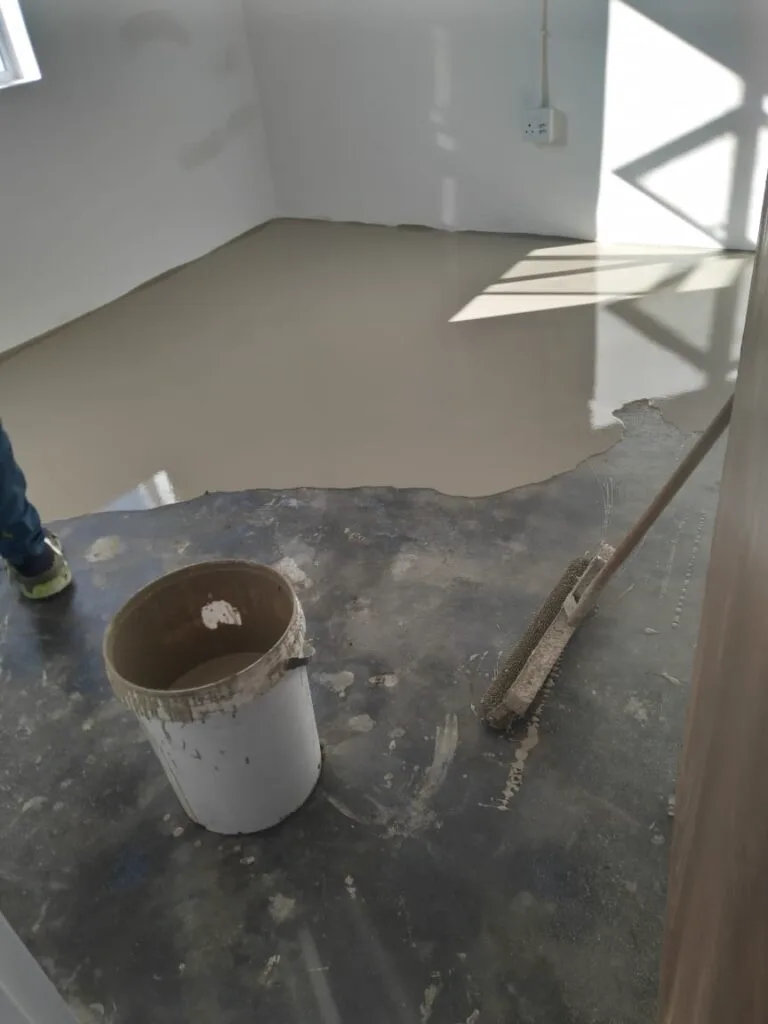 Self-levelling epoxy floor coating spreading across a bare concrete slab in a bright interior room