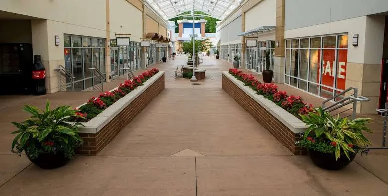 Brick raised planter beds filled with red annual flowers lining a covered retail mall walkway