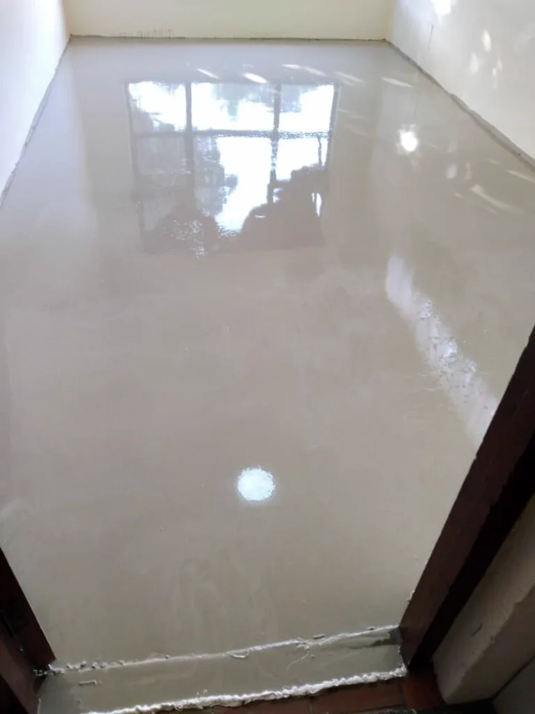 Freshly poured gloss epoxy floor reflecting a window across an empty room with a timber threshold