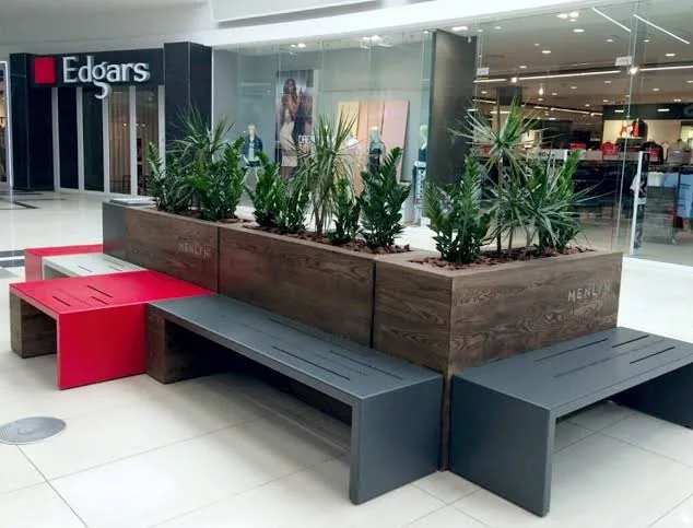 Long timber planter beds with aloes and dracaenas set between steel and concrete benches in a mall concourse