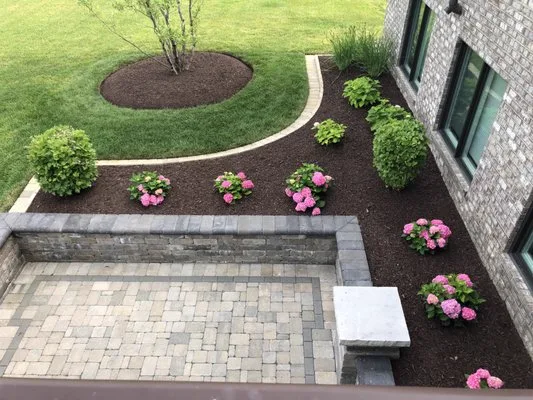 Cobble-paved patio with a stone retaining wall, bench and mulched beds of hydrangeas beside a lawn