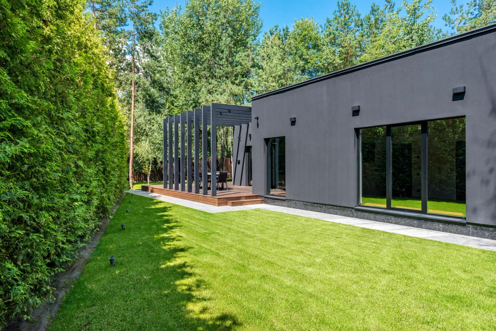 Level lawn edged with concrete paving running alongside a modern house and raised timber deck