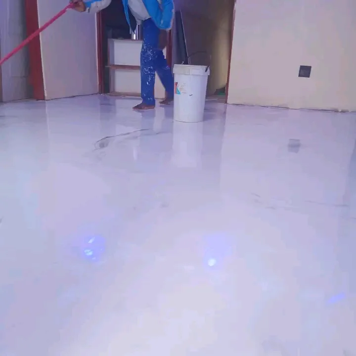 Installer applying a pearl white epoxy floor coating with a spiked roller in an interior room